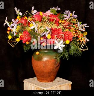 Decorating a living space with a beautiful red and green floral still life with fir branches in an old brown clay jug on a dark background. Stock Photo