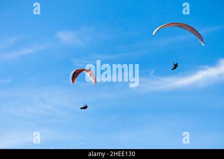 Two paragliders on parachutes flying in blue sky. Stock Photo