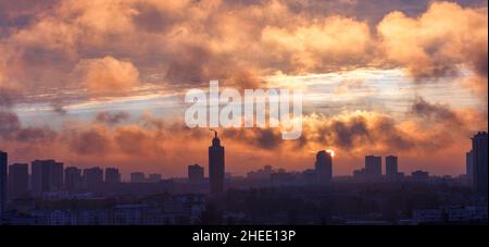 The rays of the rising sun break through the smoky smog above the silhouettes of city houses in the early morning. Copy space. Stock Photo