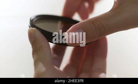 Close up of polarizing lens filter in girls hands isolated on white background. Woman turning into the both sides mechanism of lens filter. Stock Photo