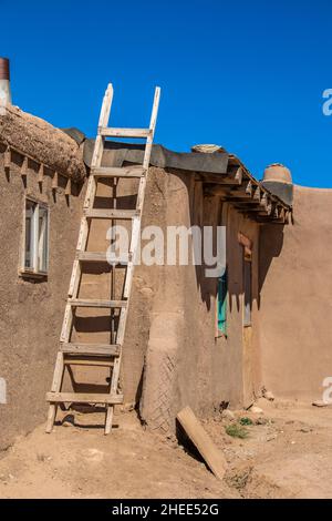 Homemade wooden ladder against side of mud adobe pueblo house where tar paper is being put on roof - with dramatic shadows under intense blue sky Stock Photo