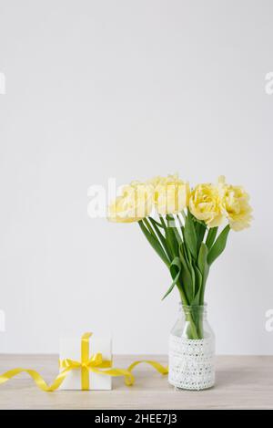 A gift box with a bow in the workplace with bouquets of bright yellow flowers and a stack of notebooks or books. Flowers for a business woman. A gift Stock Photo