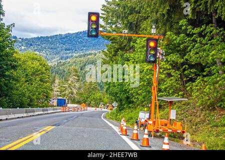 Portable solar powered traffic light at construction site in tree covered mountains with equipment and traffic cones Stock Photo