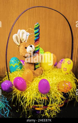 Soft plush bunny toy holding swirled candy stick in basket of Easter eggs - Selective focus Stock Photo