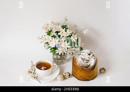 Easter card. A cake, a cup of tea, primroses in a vase and quail eggs on a light background Stock Photo