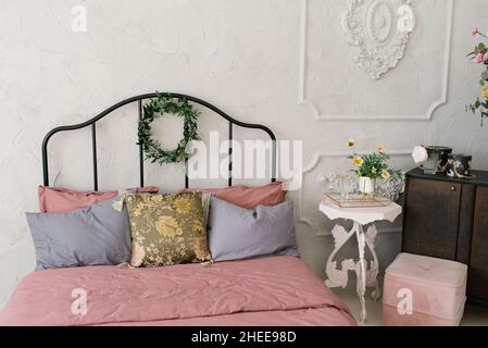 Bed with pink linens and gray pillows, a wreath of leaves on the bed Stock Photo