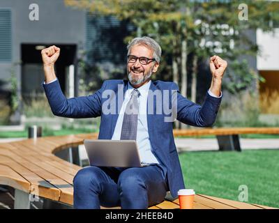 senior businessman office building laptop outdoor city celebrating success victory Stock Photo