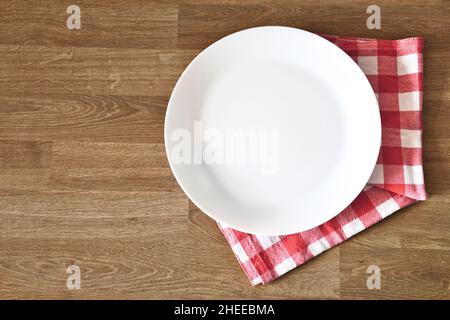 Empty white plate and towel over wooden table background. Copy space and place for meal. Top view. Stock Photo