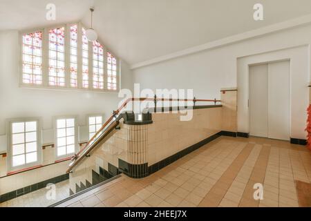 Interior of spacious hall with tiled walls and floor and staircase with handrails and glass windows with mosaic elements Stock Photo