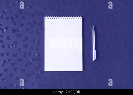 White notepad with silver pen on background with heart shaped confetti. Toned in trendy color of year 2022. Trendy template for your design in flat lay style. Copy space. Stock Photo