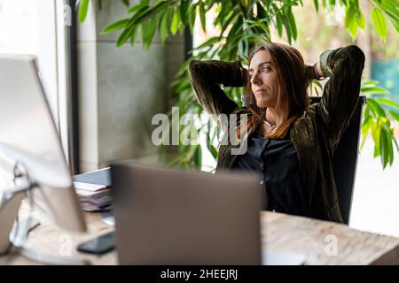 Pensive female worker sitting at wooden desktop with various documents and computer while working in light modern office Stock Photo