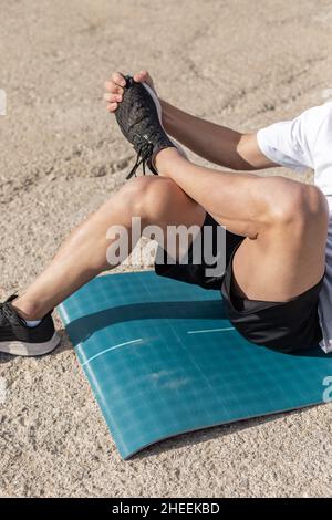 Anonymous fit sportive man in activewear doing stretching exercise on mat during training Stock Photo
