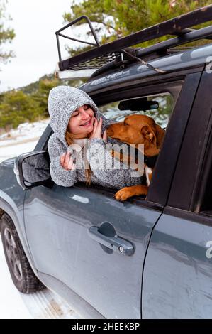 Woman sitting on driver seat caressing dog through opened window in parked car in frosty winter day Stock Photo