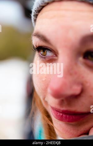 Closeup of young female wearing woolen knitted hat and warm scarf and mittens with teardrop on eye in frozen winter day Stock Photo