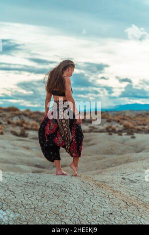 Side view of happy and optimistic lady in straw hat sitting in front of seashore cliffs and smiling away in sunset light Stock Photo