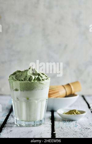 Glass of fresh dalgona coffee with matcha and Japanese tea ceremony accessories consisting of bamboo whisk called chasen placed on wooden table Stock Photo