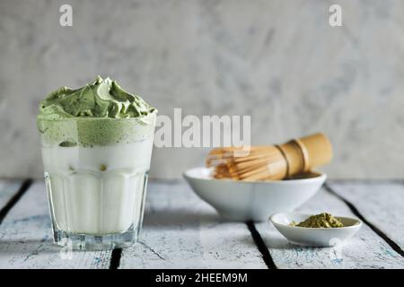 Glass of fresh dalgona coffee with matcha and Japanese tea ceremony accessories consisting of bamboo whisk called chasen placed on wooden table Stock Photo