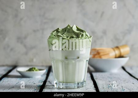 Glass of fresh dalgona coffee with matcha and Japanese tea ceremony accessories consisting of bamboo whisk called chasen placed on wooden table Stock Photo