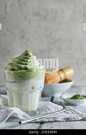 Glass of fresh dalgona coffee with matcha and Japanese tea ceremony accessories consisting of bamboo whisk called chasenand straw placed on wooden tab Stock Photo