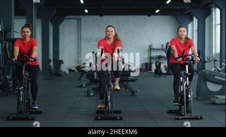 Group athletic girls performing aerobic riding training exercises on cycling stationary bike in gym Stock Photo