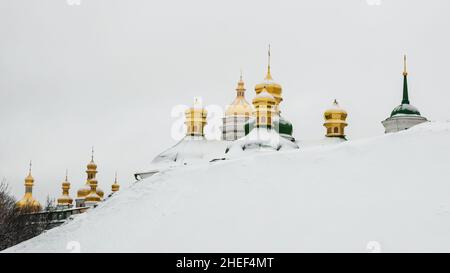 Golden domes of Kiev Pechersk Lavra or Kyiv Monastery of Caves behind a snowy slope on cold winter day. Cupolas of famous orthodox church on Dnipro Stock Photo