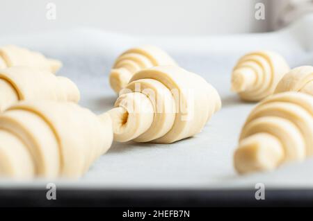 Semifinished or unbaked croissant on a baking sheet. Puff pastry baking. Close up. Stock Photo