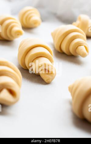 Semifinished or unbaked croissant on a baking sheet. Puff pastry baking. Close up. Stock Photo