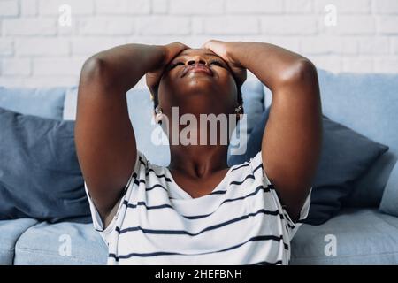 Closeup ortrait of an exhausted african american woman grabbing her head feeling stress, suffering from headaches. Stock Photo