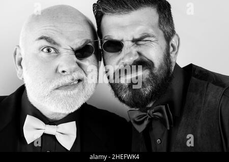 Father and bearded son are fooling around. Glasses for two. Men in suits and bow ties. Soul mates. Family business. Family traditions. Isolated on a l