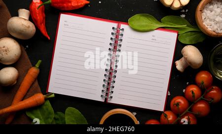 A blank recipe book template with fresh organic vegetables and a cup of seasoning on black background. Top view Stock Photo