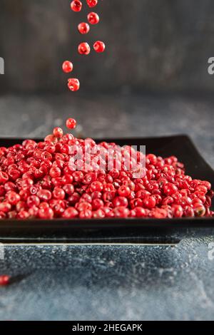 Pour red peppercorns on top of plate of pepper Stock Photo