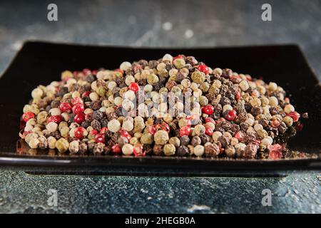 Multi-colored peppercorns on black plate with reflection Stock Photo