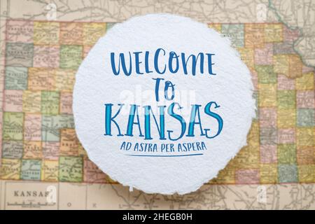 welcome to Kansas, ad astra per aspera - handwriting on a circular sheet of rough handmade paper floating over vintage defocused map of Kansas, hospit Stock Photo