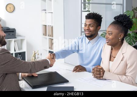 Happy young African man shaking hand of Caucasian male lawyer after signing important documents and making deal Stock Photo