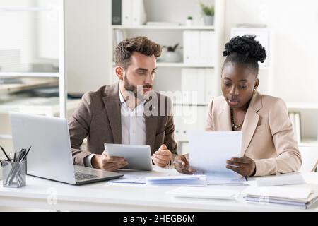Contemporary lawyer with tablet explaining points of financial paper to young African female client during consultation Stock Photo