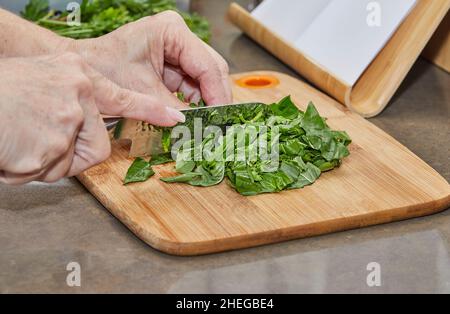 Cook cuts the basil into small pieces on wooden board Stock Photo