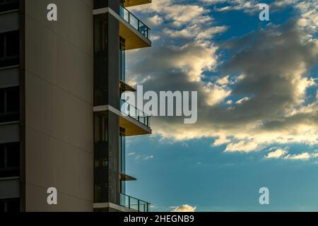 A modern high building with balconies against sunset sky and beautiful orange light sunset on white clouds, space for copy and design, landscape image Stock Photo