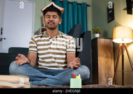 Indian student meditating by placing book on head while reading or praparing for examination at home - concept of stress relief, maditation and Stock Photo