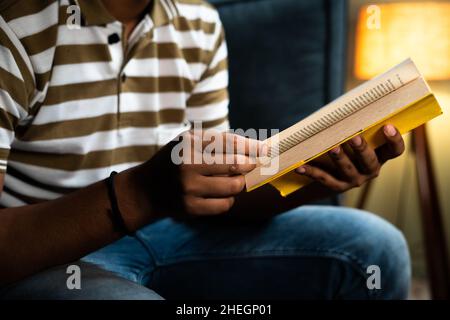 Focus on book unrecognazible young man studying book before going to sleep - concept of novel reading hobby, aspirant and bedtime reading Stock Photo