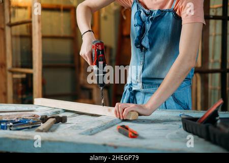 Woman working with wood in workshop. Drilling holes in timber. Reuse, reduce, recycle old things. Aware consumption and gender equality. Tools to Stock Photo