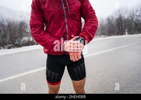 midsection of man standing outdoor in winter day checking his smart wristwatch for time and hart-rate while training outdoor male athlete runner using Stock Photo