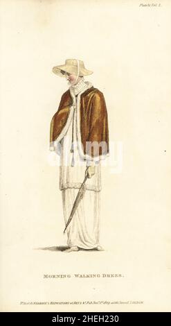 Regency woman in morning walking dress, 1809. Petticoat and Roman tunic of fine cambric, jubilee cloak of amber velvet, trimmed with swansdown, tied with silk and gold cord and tassels. Cottager's hat of imperial-coloured straw. Plate 31, November 1809. Handcoloured copperplate engraving by Thomas Uwins from Rudolph Ackermann's Repository of Arts, London. Stock Photo