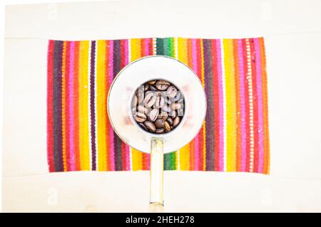 Coffee beans in vintage silver coffee making pot on colorful mat set on white table Stock Photo