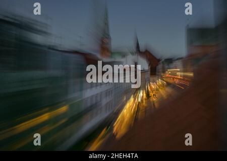 Old town dissolving in the beginning night, elderly couple still walking in the light of the shopping street, abstract blurry urban city life, long te Stock Photo