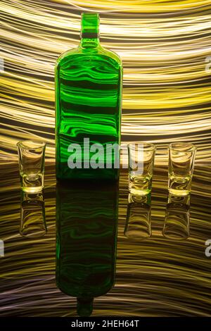 A green bottle with three shot glasses on the background which is illuminated with light painting.