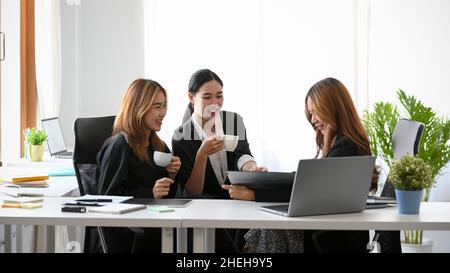 A group of a happy businesswomen or colleagues having a fun conversations, relaxed in a coffee break in the office. Stock Photo