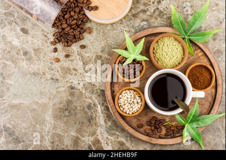 a cup of aromatic coffee with cannabis, marijuana seeds and leaves on a round wooden tray. scattered coffee beans from a glass jar. top view Stock Photo