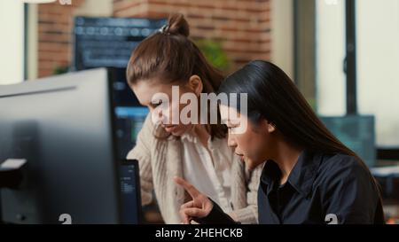 Team of software engineers talking about source code running on laptop screen while sitting at desk in it development office. Programmers collaborating on data coding group project. Stock Photo