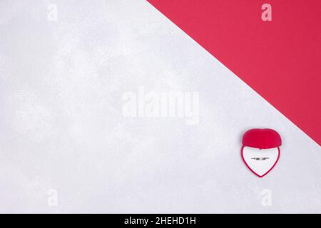 Open red velvet heart shaped gift box with wedding ring inside on red and silvery white textured background. Top view. Copy space Stock Photo