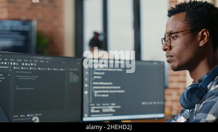 Portrait of focused software developer writing code arranging glasses sitting at desk in data room. System engineer programming user interface in busy artificial intelligence developing agency. Stock Photo